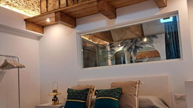 Ein Schlafzimmer mit Bett, Kissen, einem Nachttisch, einer Lampe, einem Fenster und Holzbalken an der Decke.