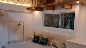 Ein Schlafzimmer mit Bett, Kissen, einem Nachttisch, einem Fenster mit Blick und Holzaufbewahrung über dem Bett.