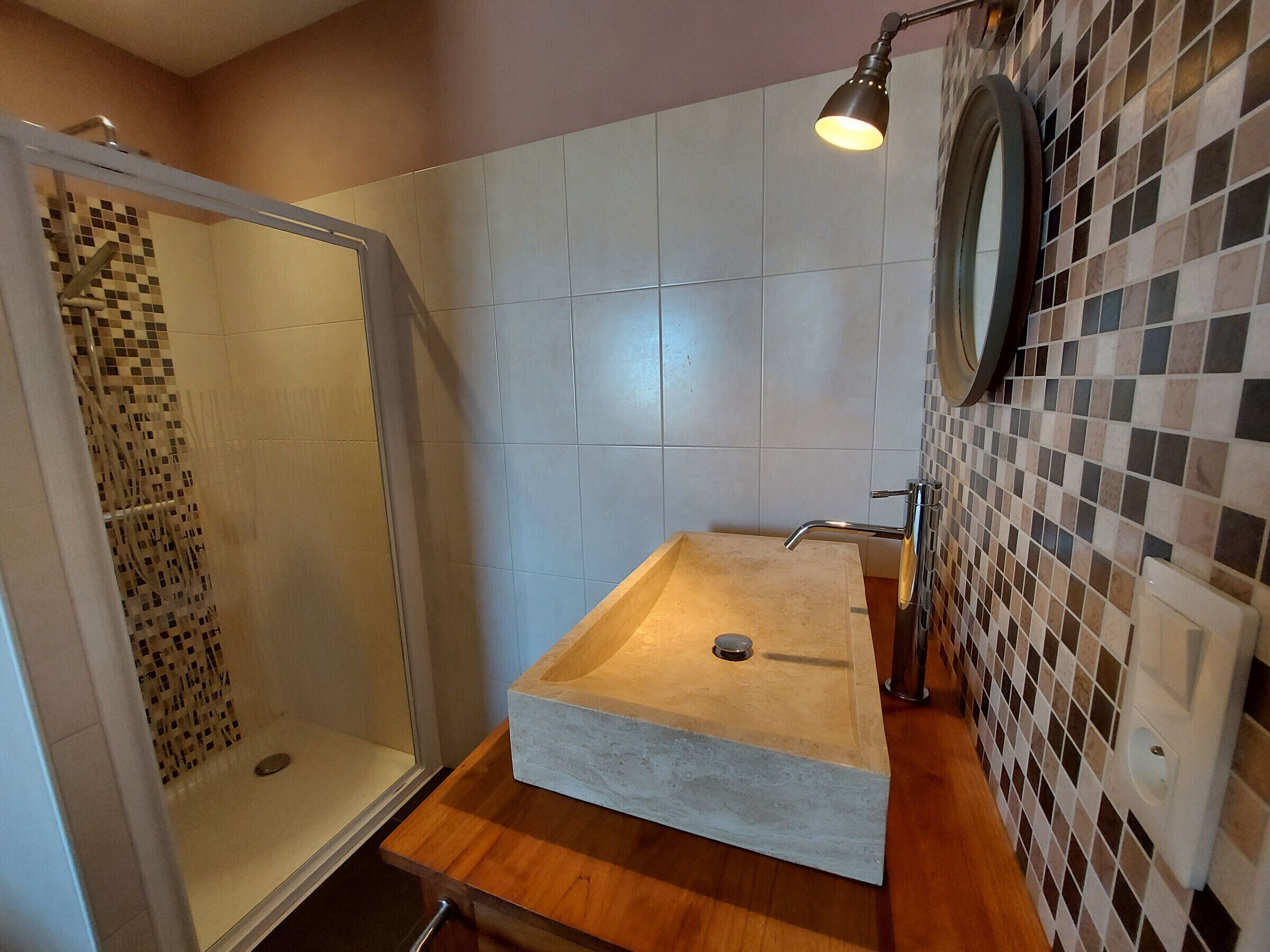 A bathroom with a glass-enclosed shower, a wooden vanity, a sink, and a tiled wall.