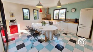 Cocina compacta con comedor, que presenta un suelo a cuadros, luces colgantes modernas y un refrigerador.