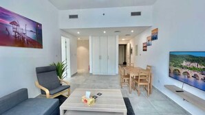 A modern living room with a sofa, coffee table, TV, and dining area. - Spacious Furnished Apartment in Palette Tower in Tourist Club Area (Abu Dhabi)