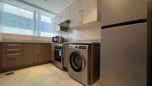 A modern kitchen with stainless steel appliances, wooden cabinets, and a large window providing natural light. - Spacious Furnished Apartment in Palette Tower in Tourist Club Area (Abu Dhabi)