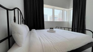 A neatly made bed with white linens in a room with black curtains, a window, and a view of buildings outside. - Spacious Furnished Apartment in Palette Tower in Tourist Club Area (Abu Dhabi)