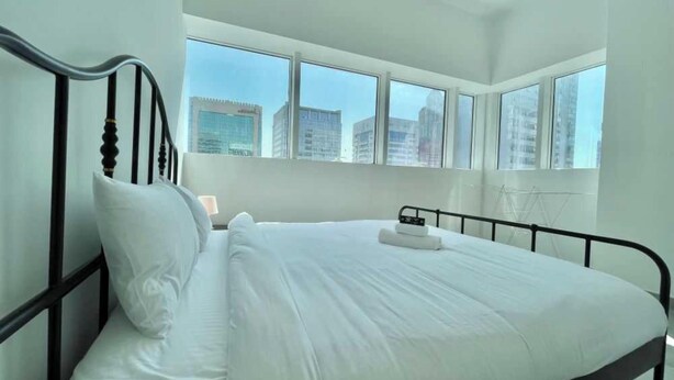 A modern hotel room with a large bed, white linens, and a city view through large windows. - Spacious Furnished Apartment in Palette Tower in Tourist Club Area (Abu Dhabi)