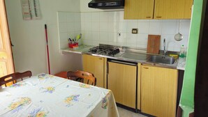 A compact kitchen with wooden cabinets, a gas stove, and a sink. There is a calendar on the wall and a table with a floral tablecloth. - Apartment with balcony (Lipari)