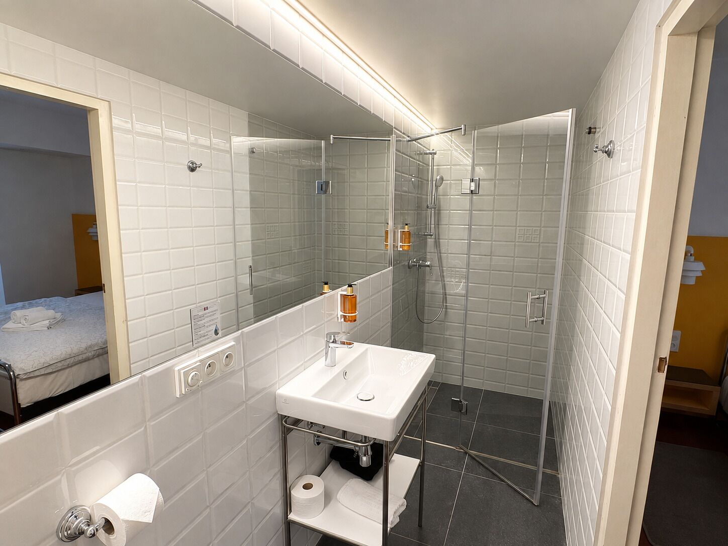 A modern bathroom with a glass-enclosed shower, a white sink, and a large mirror.