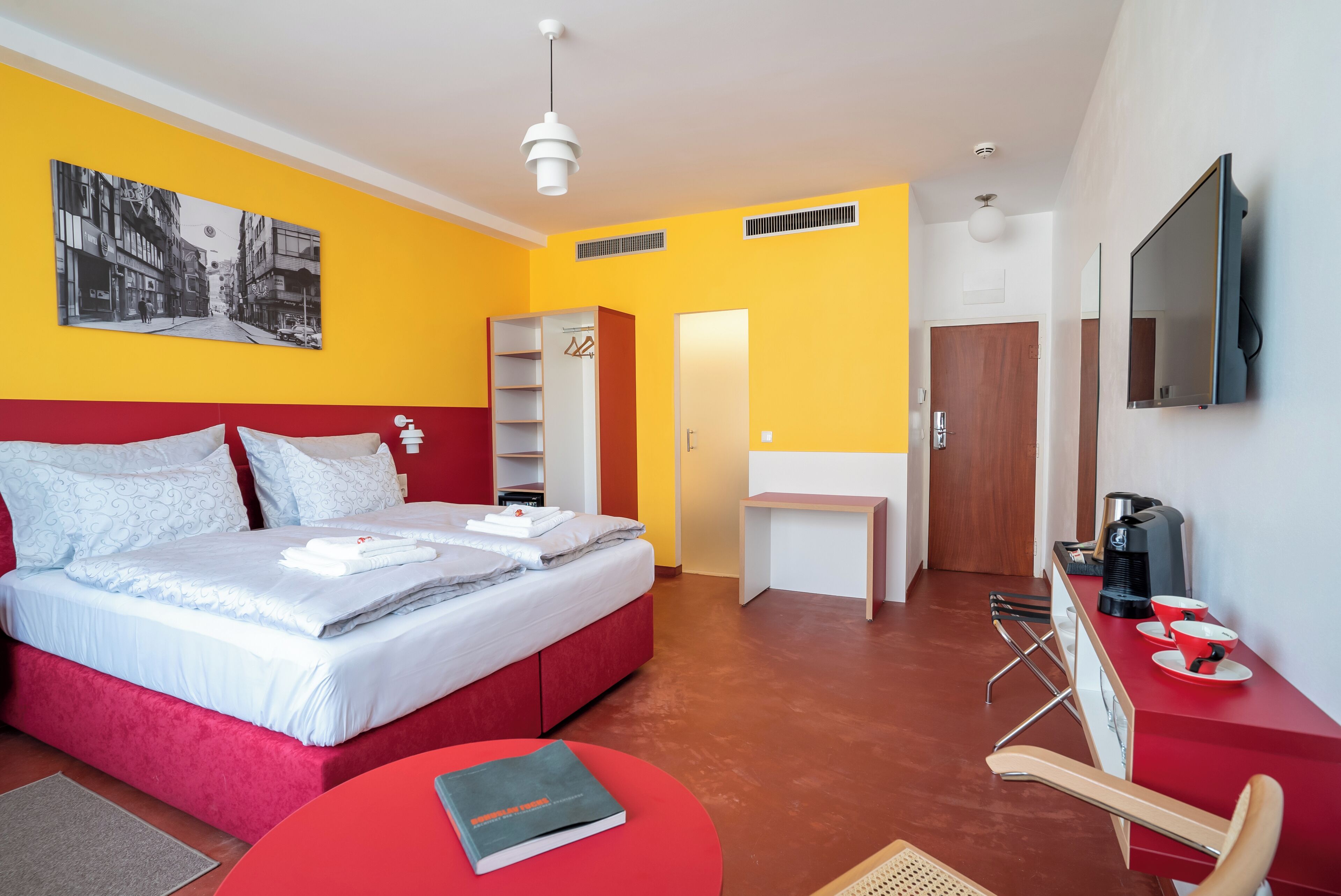 Une chambre d’hôtel moderne avec un lit rouge, un bureau, une télévision et une bibliothèque.