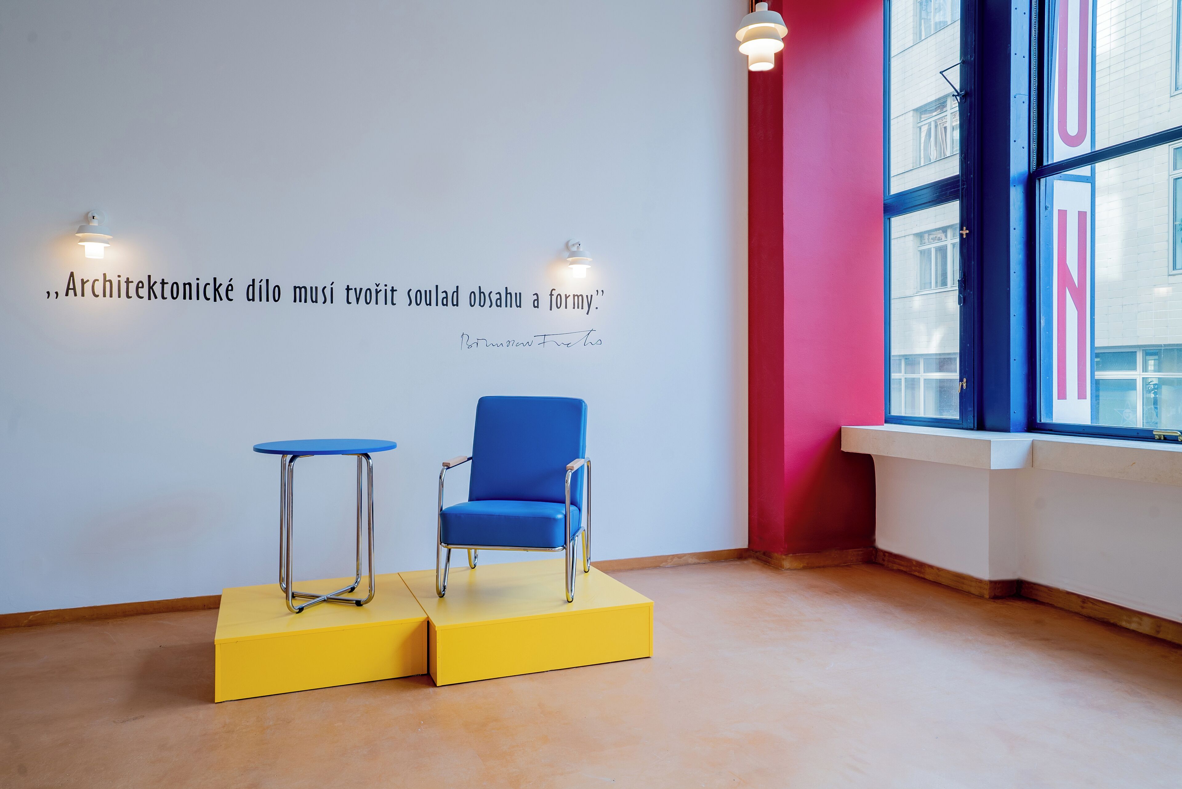 A room with a blue chair on a yellow platform, a small table, and a quote on the wall.