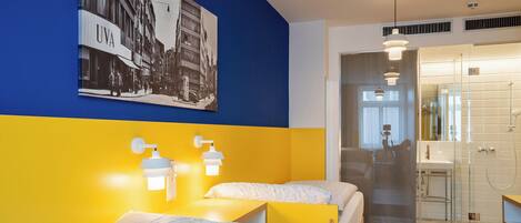 A hotel room with two beds, a bathroom with a glass shower, and a wall-mounted picture of a cityscape.