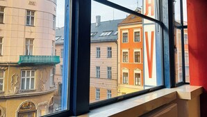 A window with a view of a building with a large 'A' sign, a radiator below, and a red wall to the right. - Hotel Avion - National Cultural Monument - ICONIC HOUSES (Brno)