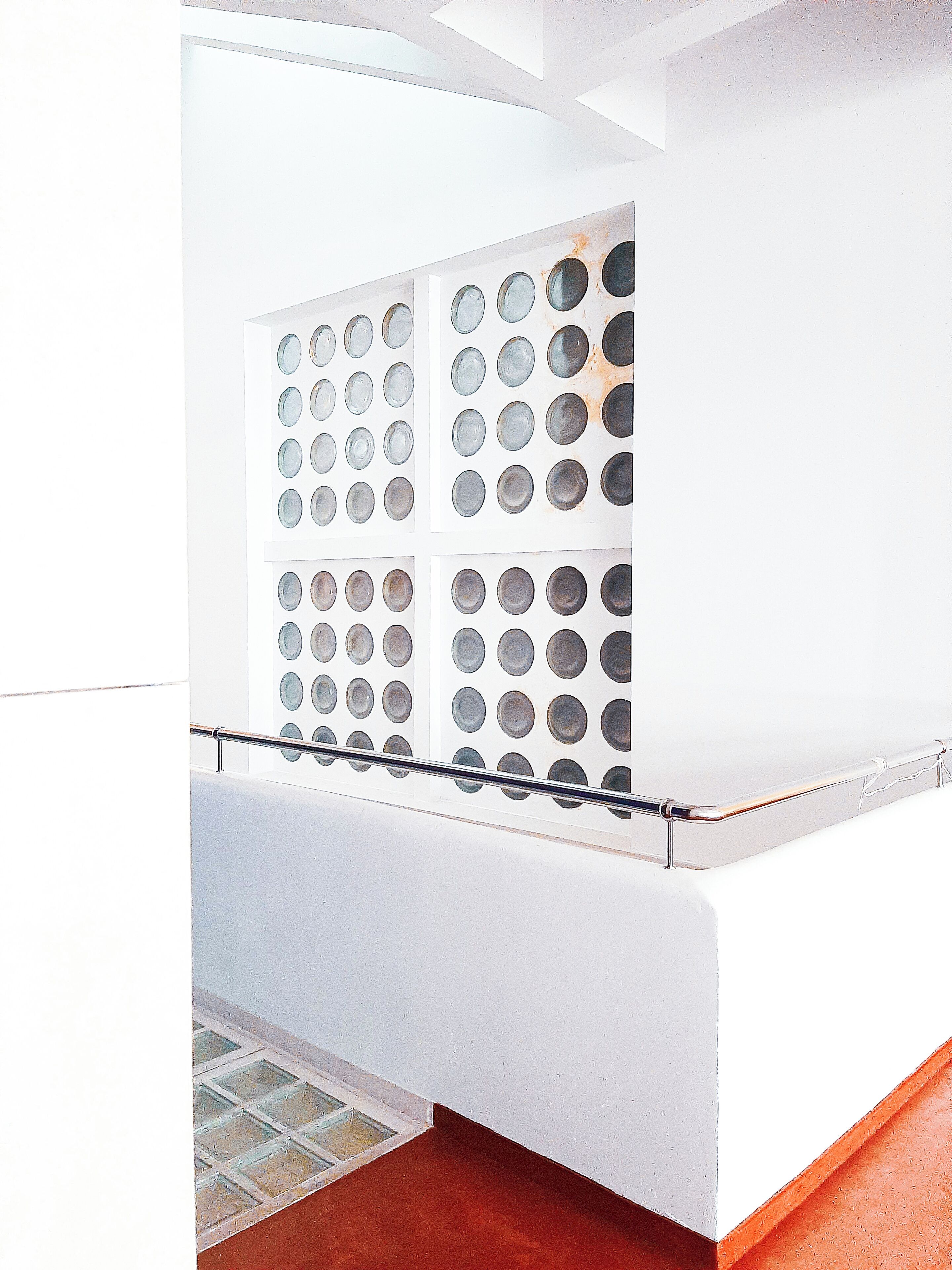 A modern bathroom with a white sink, a glass partition with circular cutouts, and a metal handrail.