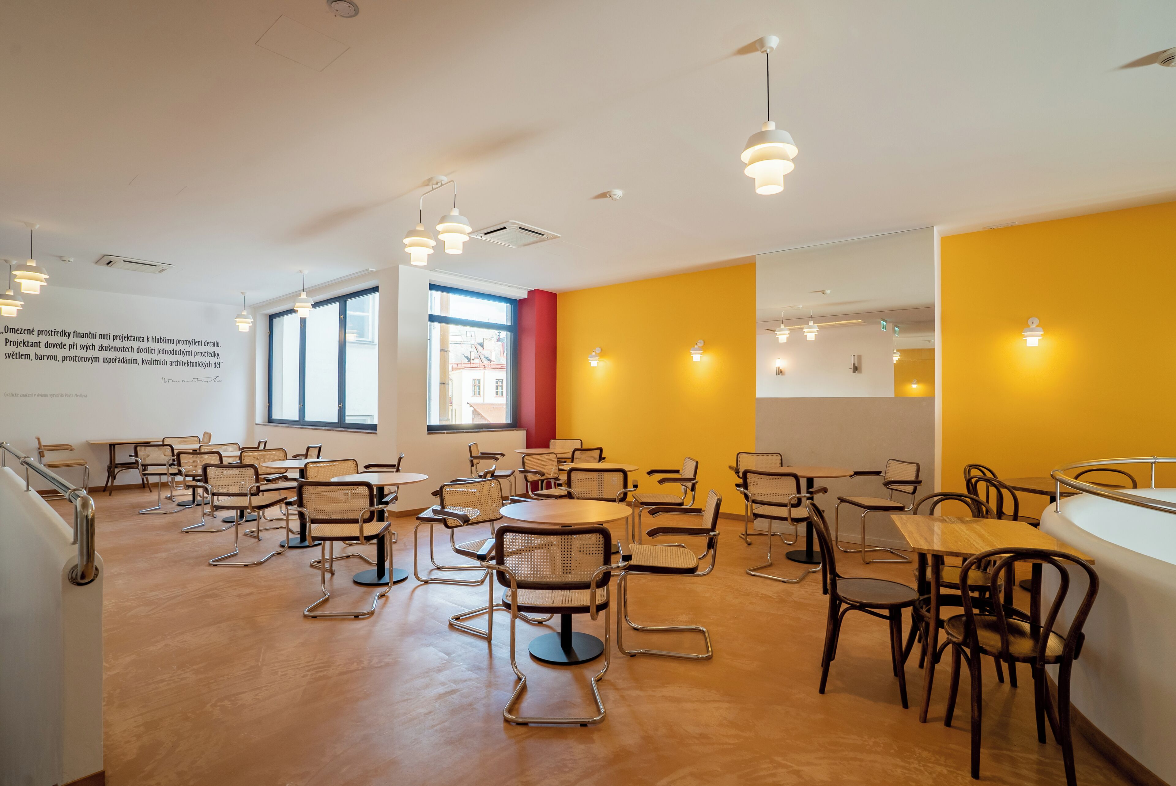 A spacious room with multiple tables and chairs, large windows, and a bright yellow accent wall.