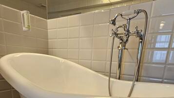 A freestanding bathtub with chrome fixtures in a bathroom with tiled walls and floor.
