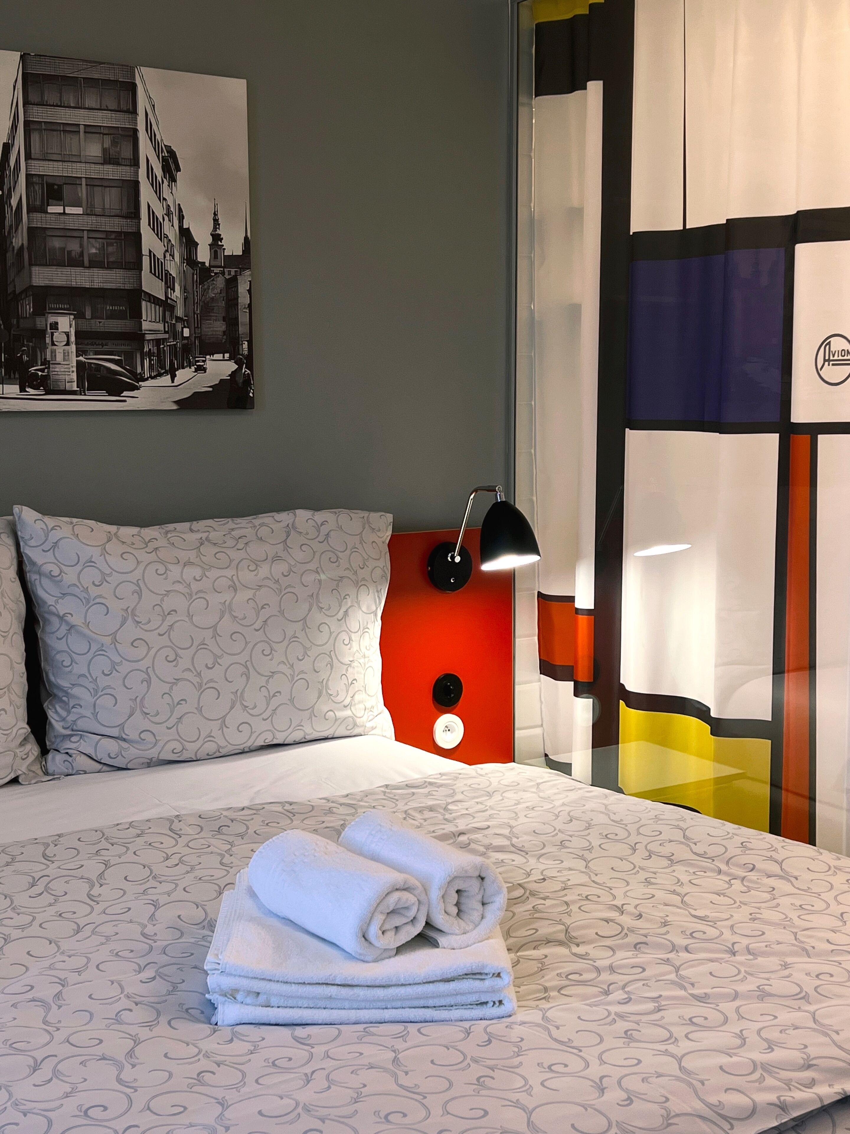 A hotel room with a bed, pillows, a lamp, and a wall-mounted painting.