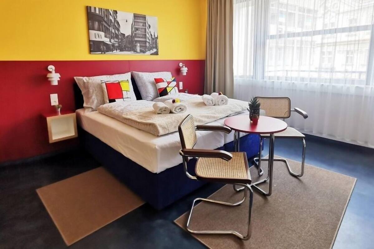 A hotel room with a bed, two chairs, a small table, and a window with curtains.