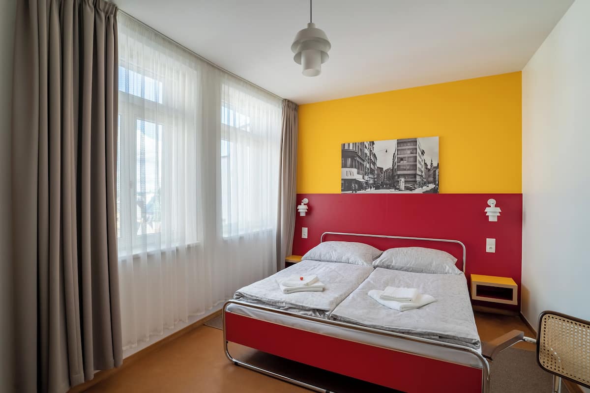 A single bed with a metal frame, a red headboard, and a small bedside table with a lamp.