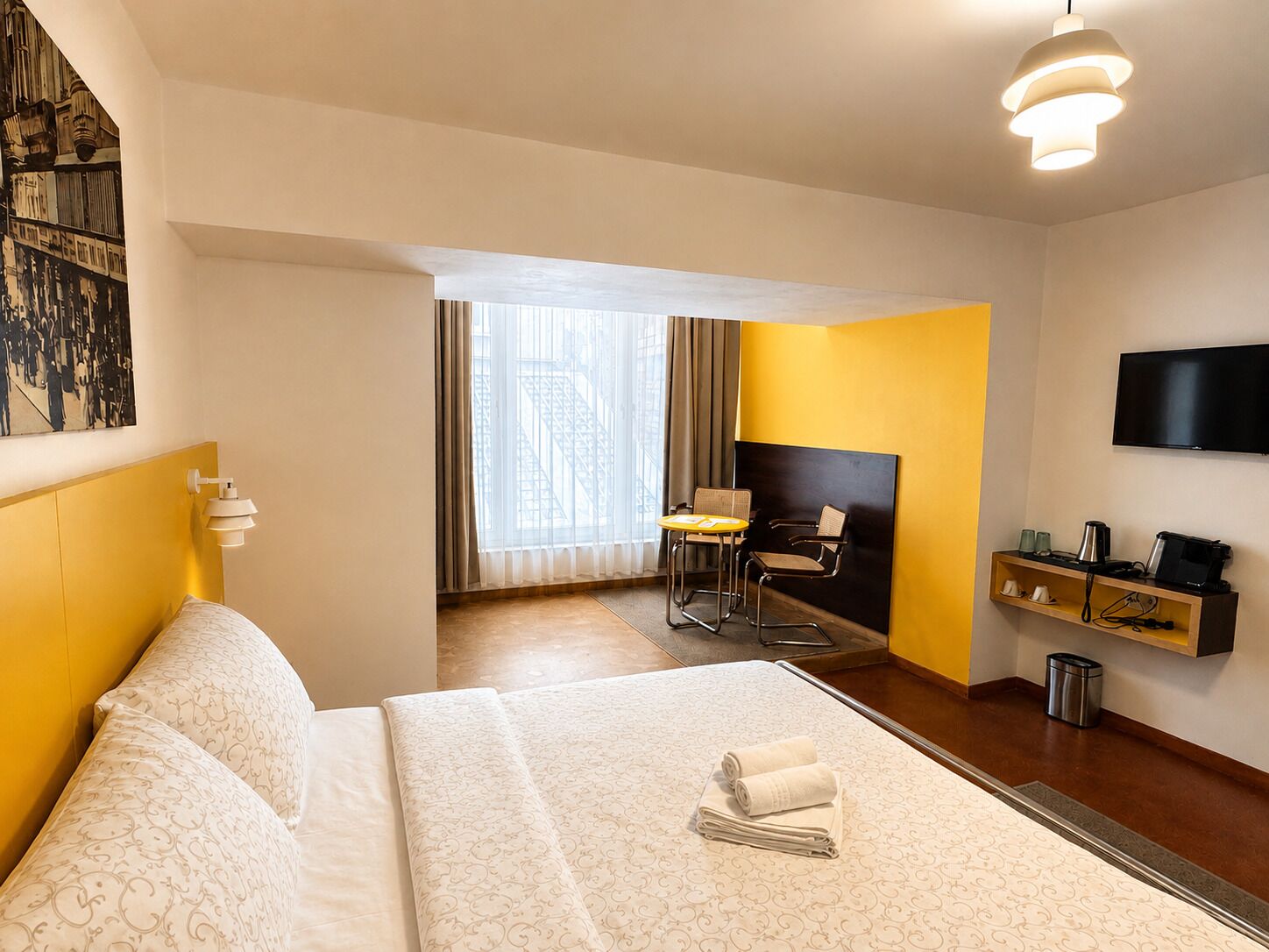Une chambre d’hôtel comprenant un lit, un bureau, une chaise, une télévision et une étagère avec quelques objets.