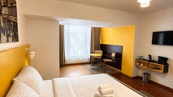 Une chambre d’hôtel comprenant un lit, un bureau, une chaise, une télévision et une étagère avec quelques objets.