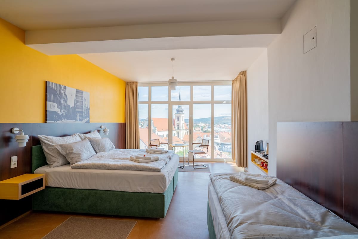 A hotel room with two beds, a view of a cityscape, a small table, and a chair.