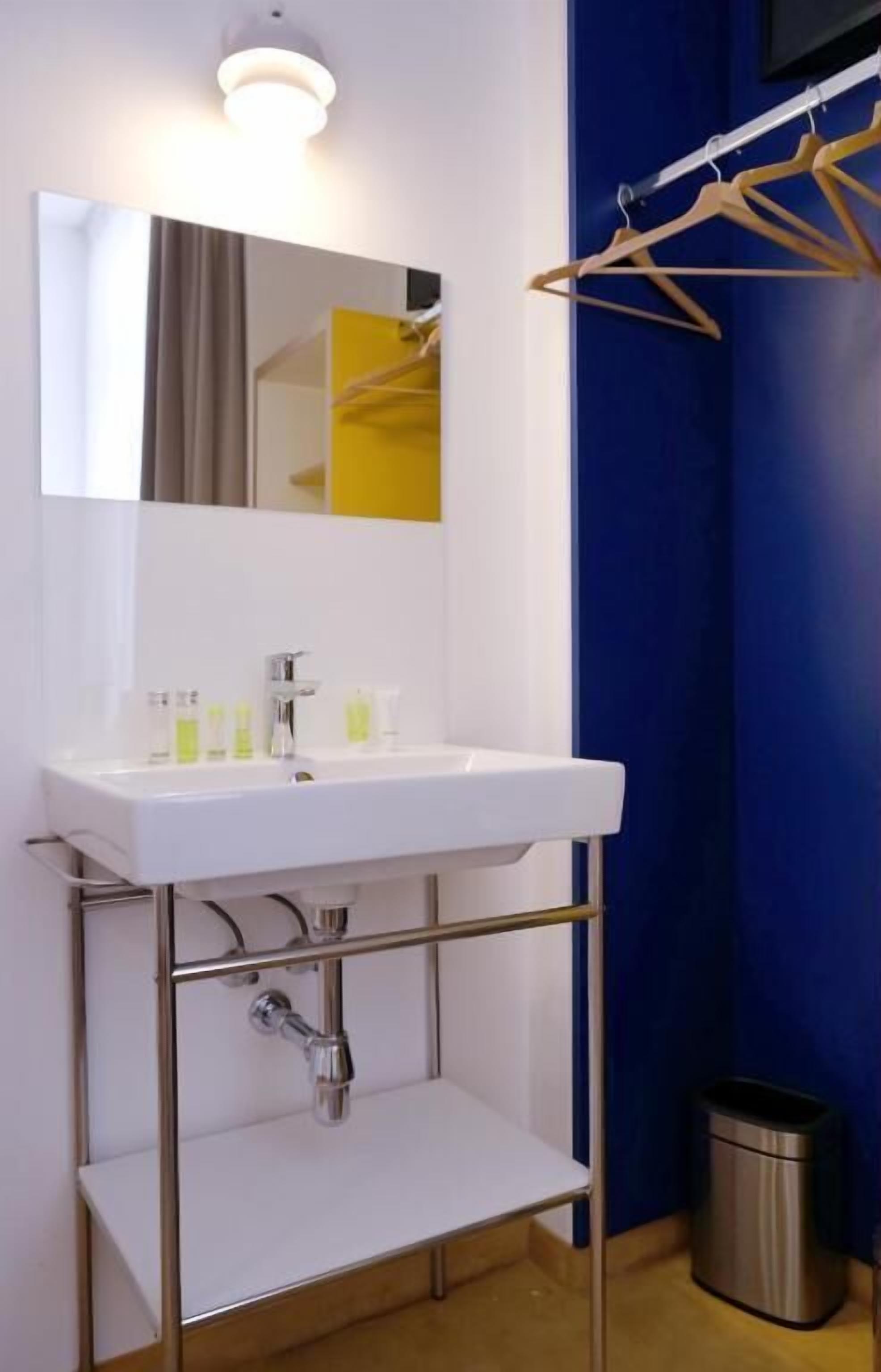 Een badkamer met een witte wastafel, spiegel en chroombeslag. De wand is blauw en er is een kledingrek.