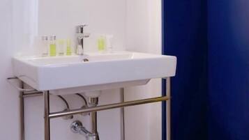 A bathroom with a white sink, mirror, and chrome fixtures. There is a blue wall and a hanging clothes rack.