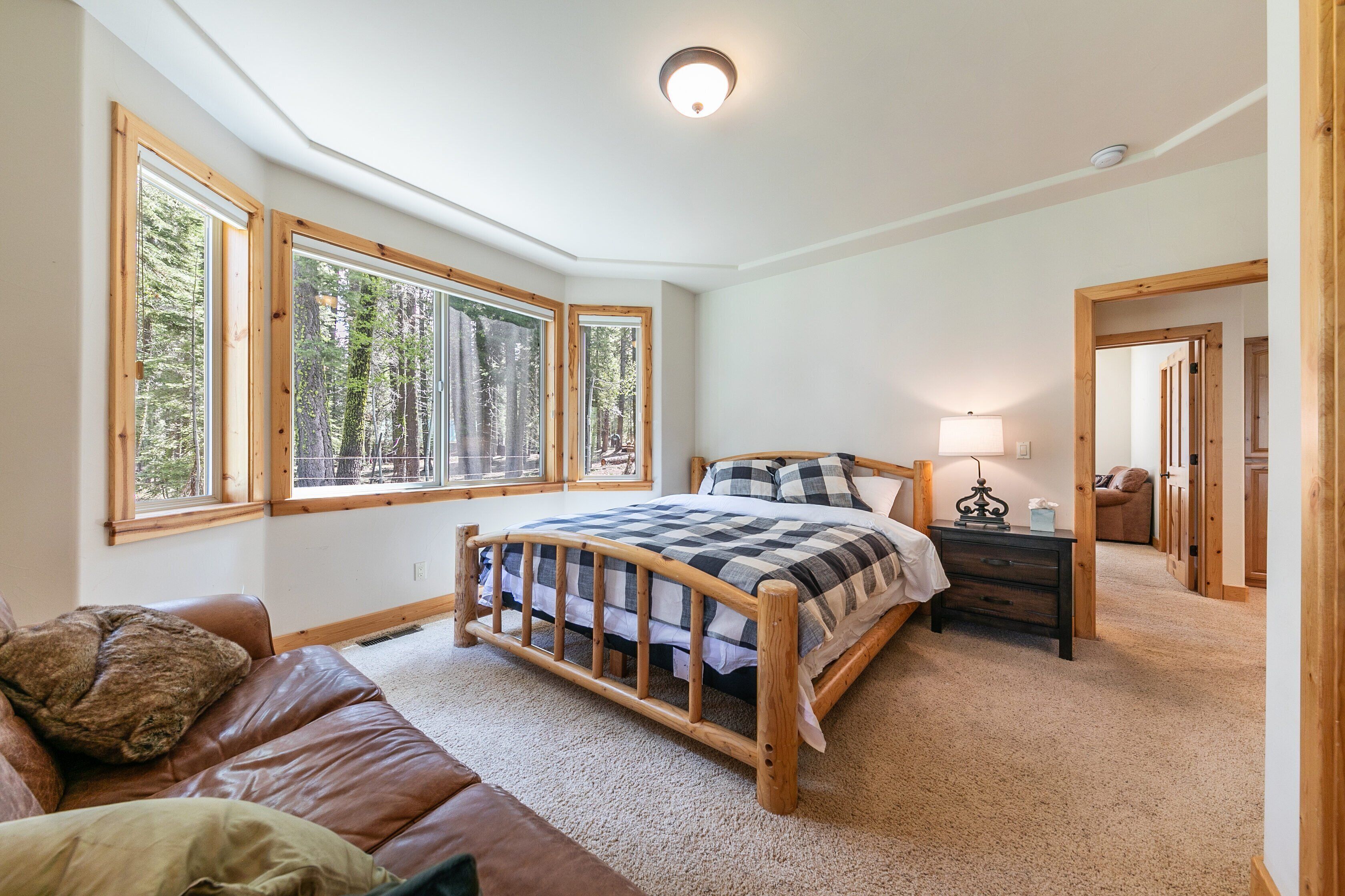 Un dormitorio con cama de madera, ventanas amplias, una mesita de noche y un espejo.