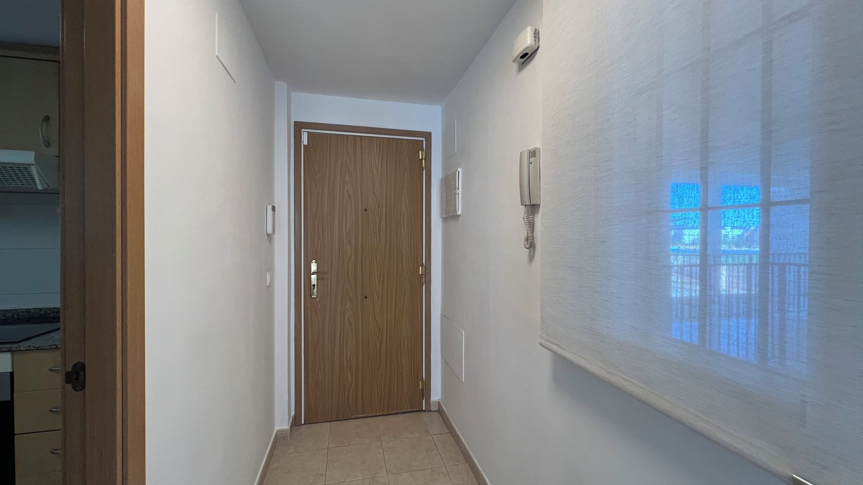 A narrow hallway with a wooden door at the end, a light switch, and a thermostat on the wall.