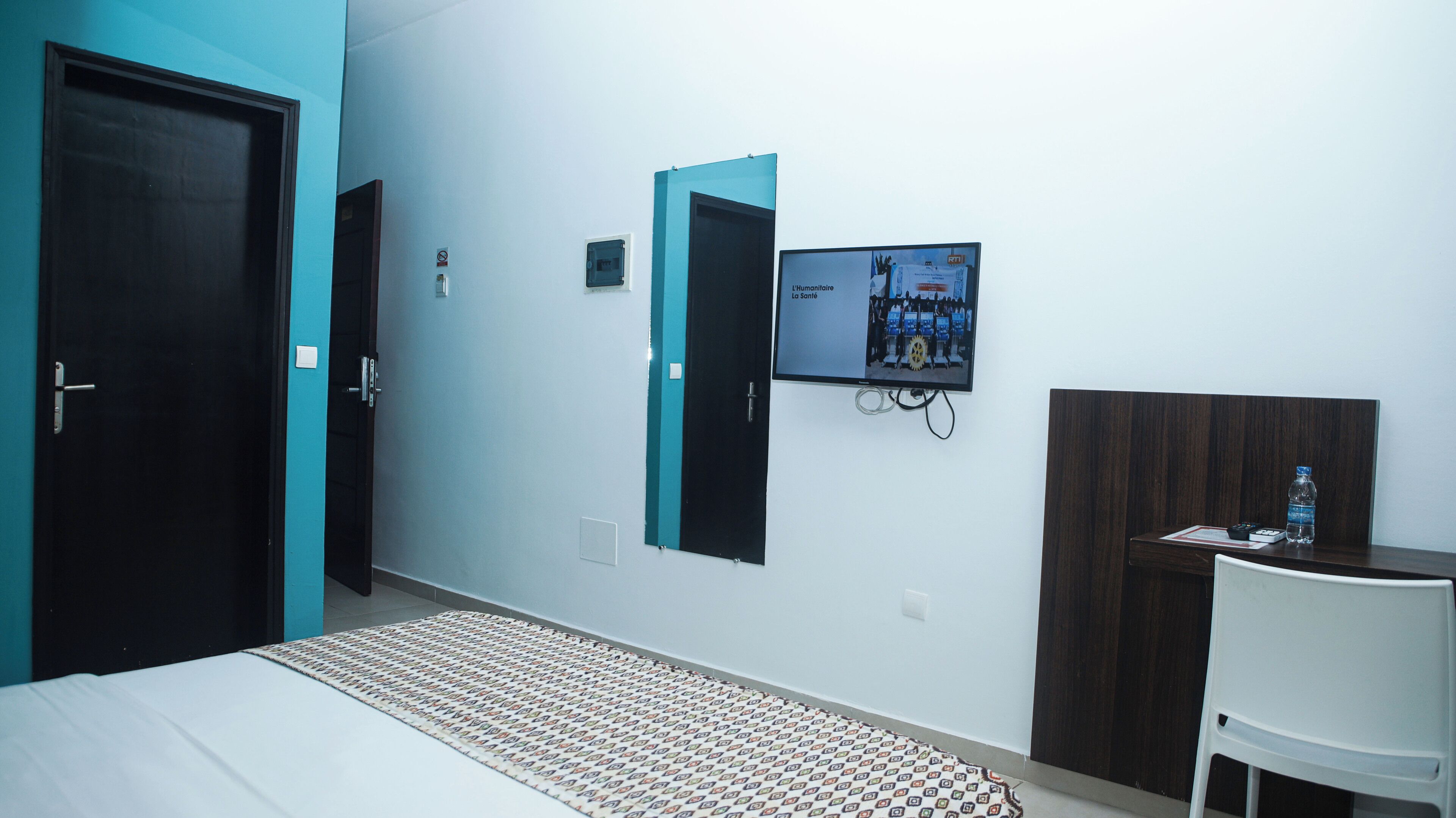 A hotel room with a bed, a desk, a chair, a TV, and two doors.