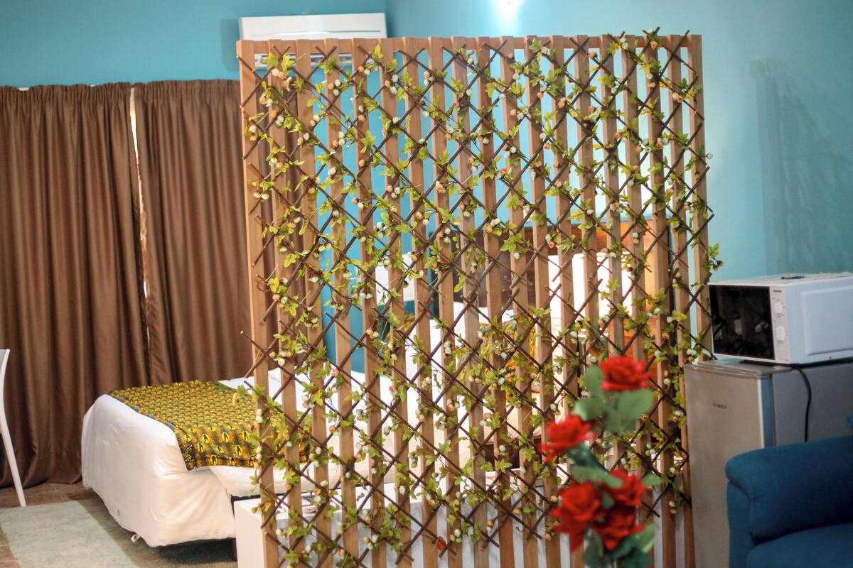 Un dormitorio con cama, escritorio, silla, televisor y una planta decorativa.