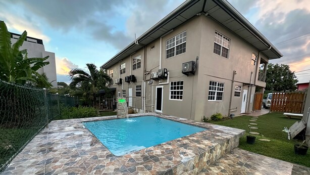 A two-story house with a swimming pool surrounded by stone tiles, a fenced yard, and a wooden deck.