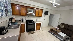 A compact kitchen with wooden cabinets, a gas stove, a microwave, and a sink. There's a small dining area with a sofa and a coffee table.