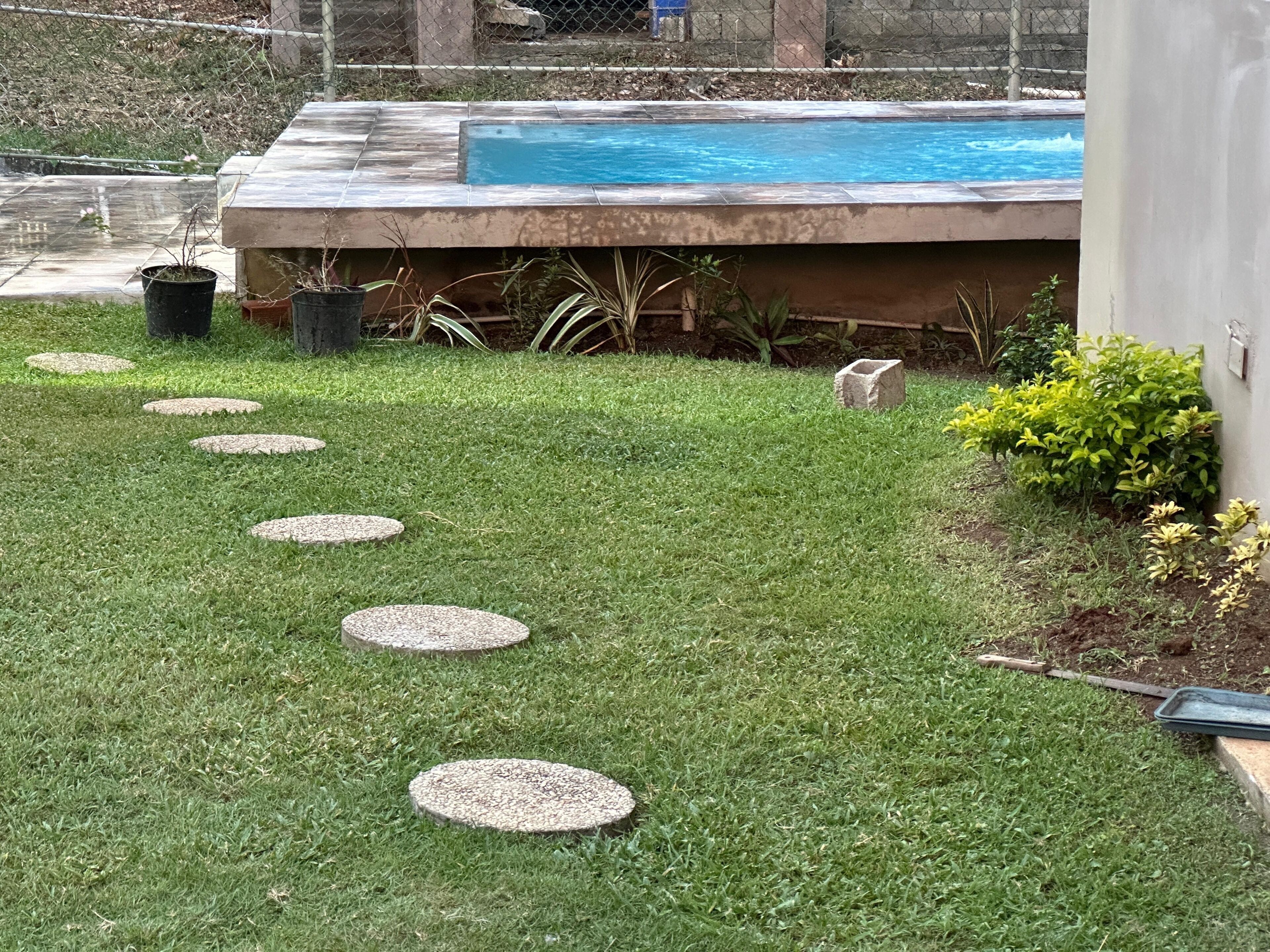 A backyard with a swimming pool, a stone pathway, and a small garden area.