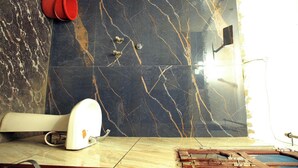 Un bagno con piastrelle di marmo scuro, un WC bianco, un secchio rosso e uno spazio doccia.