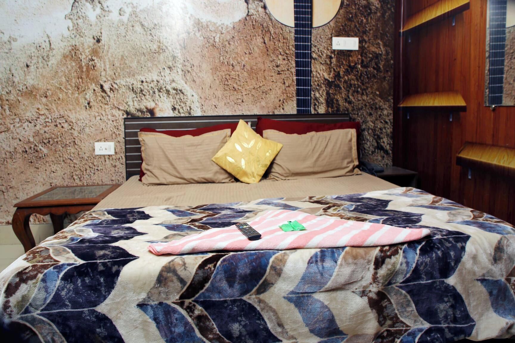 A bedroom with a bed, a guitar wall decoration, a wooden nightstand, and a wooden wardrobe.