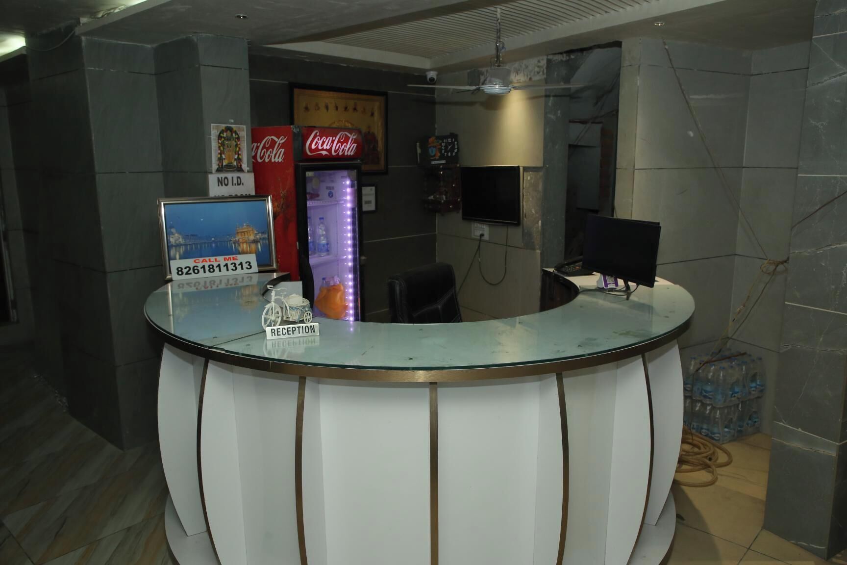 Un comptoir d’accueil avec un plateau en verre, un réfrigérateur Coca-Cola, un distributeur d’eau et un panneau indiquant un numéro de téléphone.