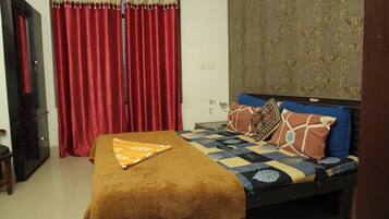 A bedroom with a bed, red curtains, a patterned wall, and a brown throw blanket.