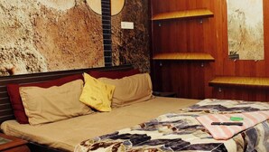 Una stanza con un letto, un'opera d'arte con una chitarra, una mensola in legno e una pianta.