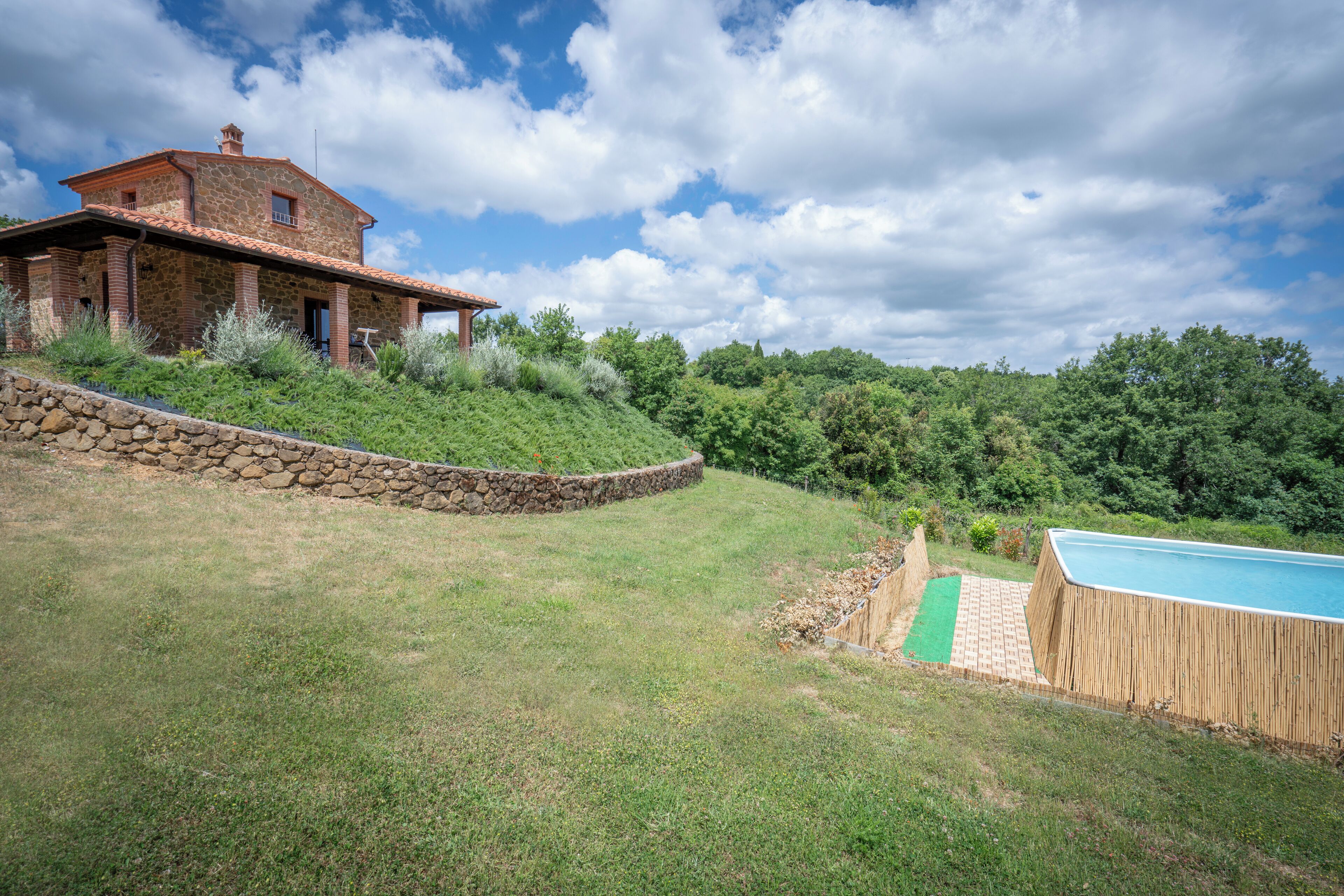 A stone house with a red-tiled roof, a swimming pool, and a stone retaining wall.