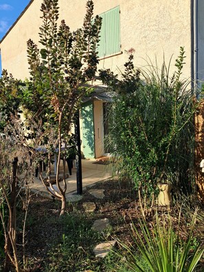 Un jardin où l’on trouve différentes espèces de plantes et un bâtiment doté d’un volet vert.