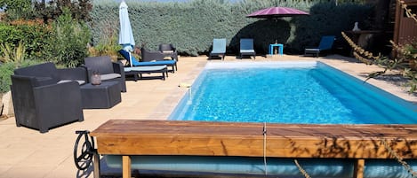 Une piscine entourée de verdure, avec des chaises longues et des parasols.