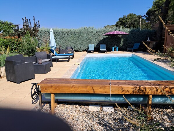 Une piscine entourée de verdure, avec des chaises longues et des parasols.