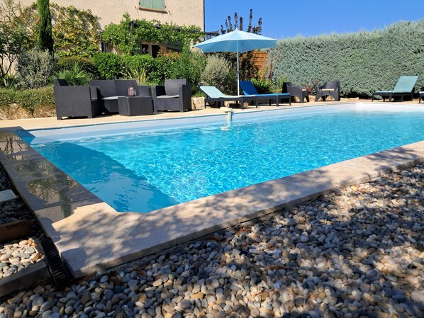 A swimming pool with lounge chairs and an umbrella.
