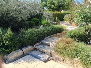 Ein gepflegter Garten mit einem Kiesweg, verschiedenen Sträuchern und einer kleinen Statue.