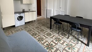 A compact living space with a kitchenette, a dining table with chairs, and a patterned floor. - Bari LandLord 242 (Bari)