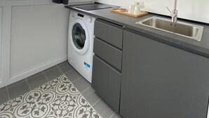 A compact kitchen with a washing machine, a sink, and a window with curtains. - Bari LandLord 242 (Bari)