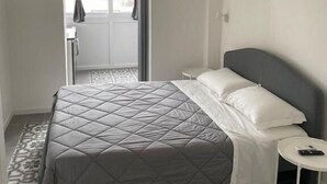 A hotel room with a bed, a small bedside table, a window with curtains, and a patterned floor. - Bari LandLord 242 (Bari)