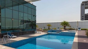 A rooftop swimming pool with lounge chairs and a modern building in the background. - Cosmos Living Charming Studio With Balco (Dubai)