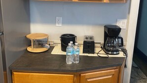Eine Küche mit Holzausstattung, einer Arbeitsplatte, einem Toaster, einer Kaffeemaschine und zwei Wasserflaschen.