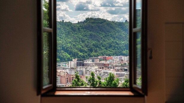 Uma janela com vista para um horizonte urbano e uma colina com árvores.
