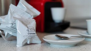 Uma máquina de café, uma colher e sachês de café cremoso em uma bancada.